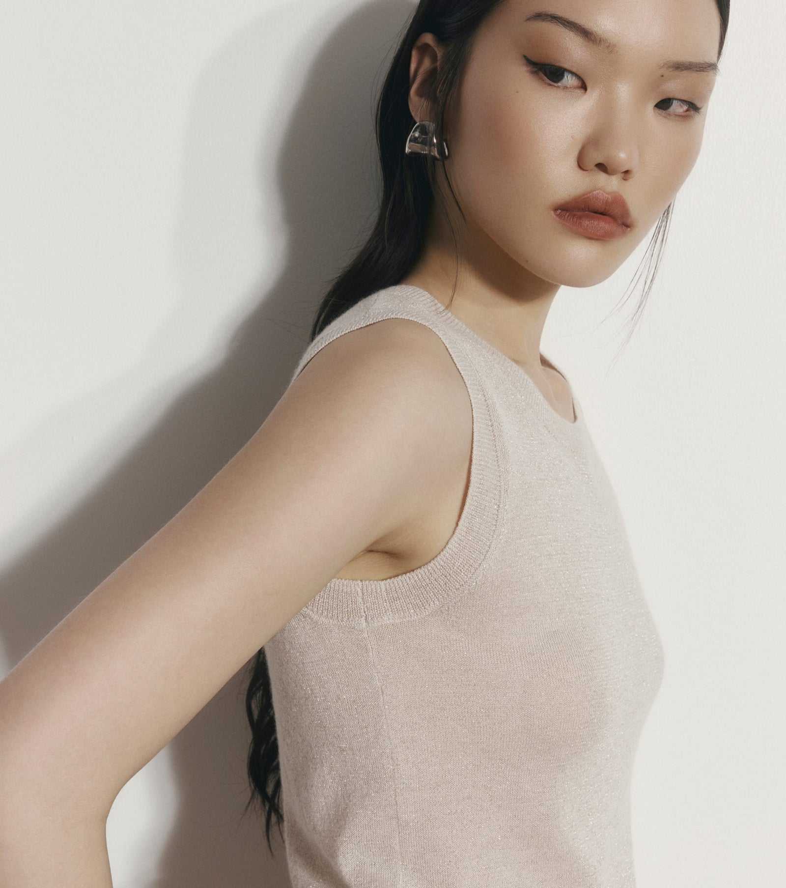 Woman wearing a beige sleeveless top against a plain background